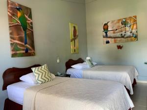 two beds in a room with paintings on the wall at Hotel Nahomi Divisamar by LHR in Manuel Antonio
