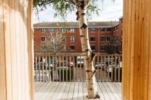 a tree in front of a fence with a building at Carmen Eco-Pod / Treehouse, Close to Cabot Circus in Bristol