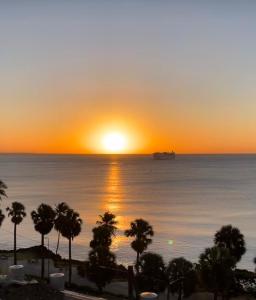 una puesta de sol sobre el océano con palmeras y un barco en Hotel Shakey en Santo Domingo