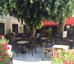 un patio con mesas y sillas bajo un árbol en Hotel de Paris, en Le Bugue