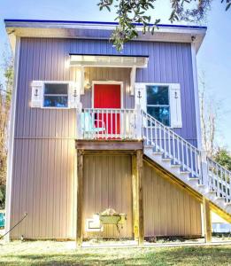 a small house with a red door and a balcony at Secluded Tiny House by the Marsh with Hunting Island Beach Pass in St. Helena Island