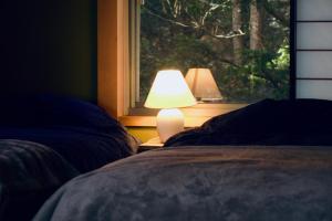 1 dormitorio con ventana y lámpara junto a 2 camas en 天然温泉付き プライベート空間 北アルプスの麓安曇野 貸切一棟貸 70型スクリーン完備 フモトノイエ, en Azumino