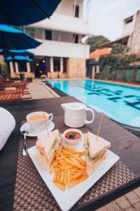 a sandwich and french fries on a table next to a pool at St.Lachlan Hotel & Suites in Negombo