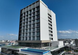a tall white building with a pool in front of it at HOTEL AlaCOOJU OKINAWA in Urazoe
