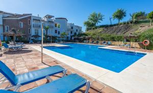 una gran piscina con sillas y sombrillas azules en Los Eucaliptos Appartement deux chambres Chez Stefan en Benahavís