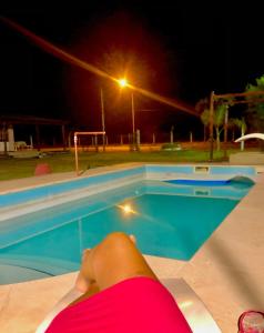 a person laying on a ledge next to a swimming pool at night at LA CABAÑA in Termas de Río Hondo