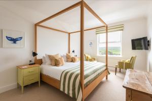 a bedroom with a canopy bed with a desk and a chair at The St Enodoc Hotel in Wadebridge