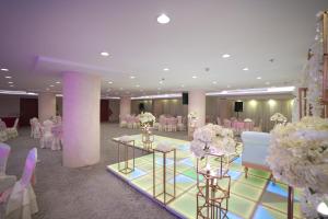 un salón de banquetes con mesas, sillas blancas y flores en La Fontaine Jeddah Hotel, en Yeda