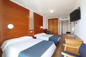 a hotel room with two beds and a desk and a television at Hotel Poseidon Playa in Benidorm