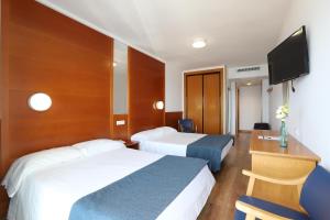 a hotel room with two beds and a desk and a television at Hotel Poseidon Playa in Benidorm