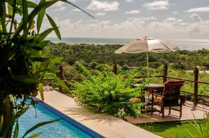 a patio with a table and an umbrella and the ocean at Pousada Mar à Vista in Trancoso