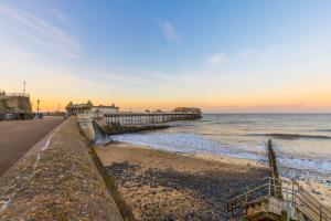 a beach with a pier and the ocean at sunset at Fishermans Cottage - Norfolk Holiday Properties in Cromer