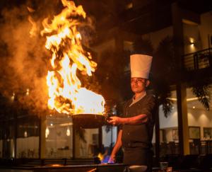 a man in a chefs hat holding a pan with fire at Cassandra Culture Resort in Sigiriya