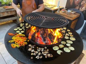 Un homme cuisine de la nourriture sur un grill avec une cheminée dans l'établissement Biohofgut LASCHALT, à Deutsch Kaltenbrunn