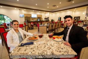 Ein Mann und eine Frau sitzen an einem Tisch mit Essen in der Unterkunft Best Western Las Mercedes Airport in Managua
