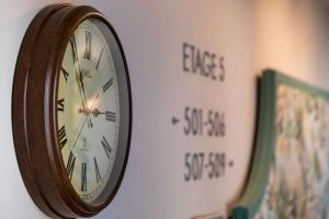 a clock hanging on a wall next to two signs at Hotel Camille Paris Tapestry Collection by Hilton in Paris