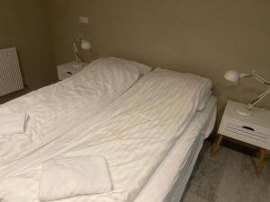a bed with white sheets and two lamps on a table at Heppa Apartments in Höfn