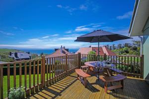 una terraza de madera con mesa y sombrilla en Cedar Lodge, en Portpatrick