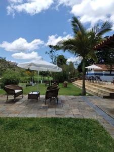 a patio with benches and an umbrella and a palm tree at Solar Azul Pousada Boutique in Miguel Pereira