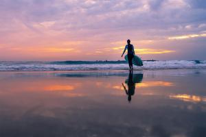 a man walking on the beach with a surfboard at Gold Coast Photography Inn in Estoril