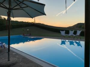 a swimming pool with two chairs and an umbrella at Casa villetta "La Colomba" Nizza Monferrato in Nizza Monferrato