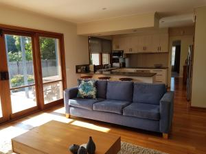 a living room with a blue couch and a kitchen at Sandy Bottoms in Point Lonsdale