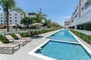 uma piscina com espreguiçadeiras ao lado de um edifício em Cannes Club Residence a 200m da praia, recém inaugurado em Florianópolis