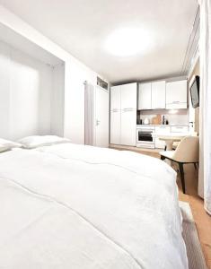 a white bedroom with a white bed and a kitchen at Bright Tiny Studio - Shared Pool & Sauna - Free Parking - Air condition in Muralto