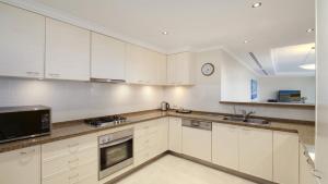 Una cocina con gabinetes blancos y un reloj en la pared. en Unit 46 - 3 Bed Ocean View, en Terrigal