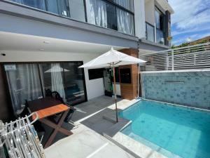 a swimming pool with an umbrella next to a house at Flat do Lucca 02 - Piscina - 50m da Praia - Até 10 Pessoas in Tamandaré