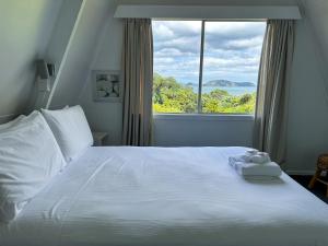 a bedroom with a white bed with a large window at Pohutukawa Coastal Chalets in Coromandel Town