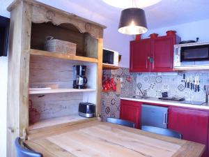 a kitchen with a wooden table and red cabinets at Studio cabine 3 couchages au pied des pistes, ascenseur, casiers à ski, parking - Auris en Oisans - FR-1-297-76 in Auris