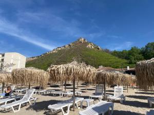 - une plage avec des chaises longues, des parasols en paille et une montagne dans l'établissement SEA Apartment Maria Balchik, à Balchik