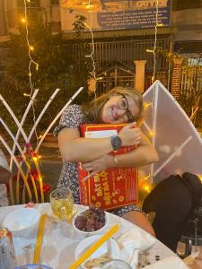 Una donna abbraccia una scatola a un tavolo di Bà Ngoại Homestay a Cà Mau