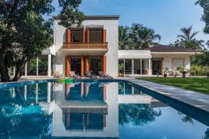 a villa with a swimming pool in front of a house at SaffronStays Hacienda by the Sea, Alibaug in Alibaug
