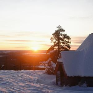 una casa cubierta de nieve con la puesta de sol en el fondo en Levin Alppitalot Alpine Chalets Deluxe en Levi