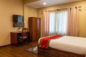een slaapkamer met een bed, een bureau en een televisie bij Kuna Resort in Kathmandu