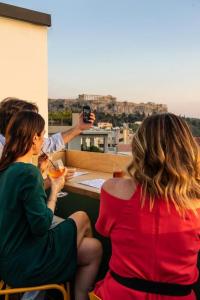 Un uomo che scatta una foto a due donne sedute a un tavolo di Mosaikon Glostel ad Atene