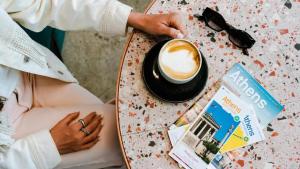 Eine Frau, die an einem Tisch mit einer Tasse Kaffee sitzt. in der Unterkunft Mosaikon Glostel in Athen