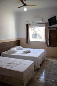 two beds in a bedroom with a fan and a window at Pousada Bela Rainha in Aparecida
