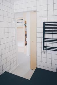 a white tiled bathroom with a door and a shelf at Blackett Street Bunkhouse in Leeds