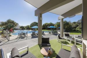 un patio con sillas, mesas y una piscina en Ramada By Wyndham Marcoola Beach en Marcoola
