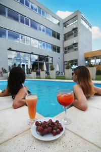 duas mulheres sentadas à beira de uma piscina com cocktails e frutas em Hotel Terra Patagonia em Malargüe