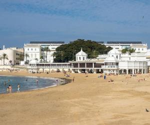 einen Strand mit Menschen im Wasser und in Gebäuden in der Unterkunft La terraza del Falla, Feel Cádiz in Cádiz
