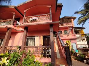 a pink house with balconies on a street at Camrose Guest House in Candolim