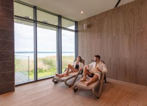 two people sitting on chairs in a room with windows at Hotel OTP Balatonszemes in Balatonszemes