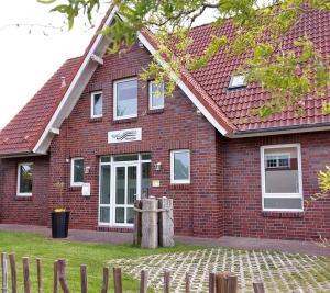 una casa de ladrillo rojo con puerta blanca en Pension Blaue Nordseewelle en Neuharlingersiel