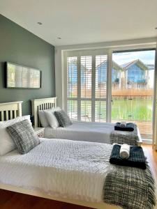 two beds in a bedroom with a large window at Luxurious Lakefront Home with Pool/Spa Access in Cirencester