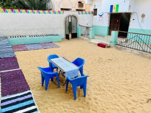 une table et quatre chaises bleues dans le sable dans l'établissement Napata Guest House, à Assouan