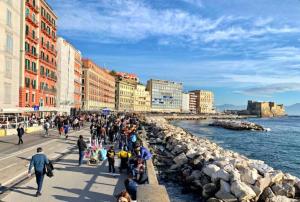 a group of people walking on a sidewalk near the water at NUVISA in Naples